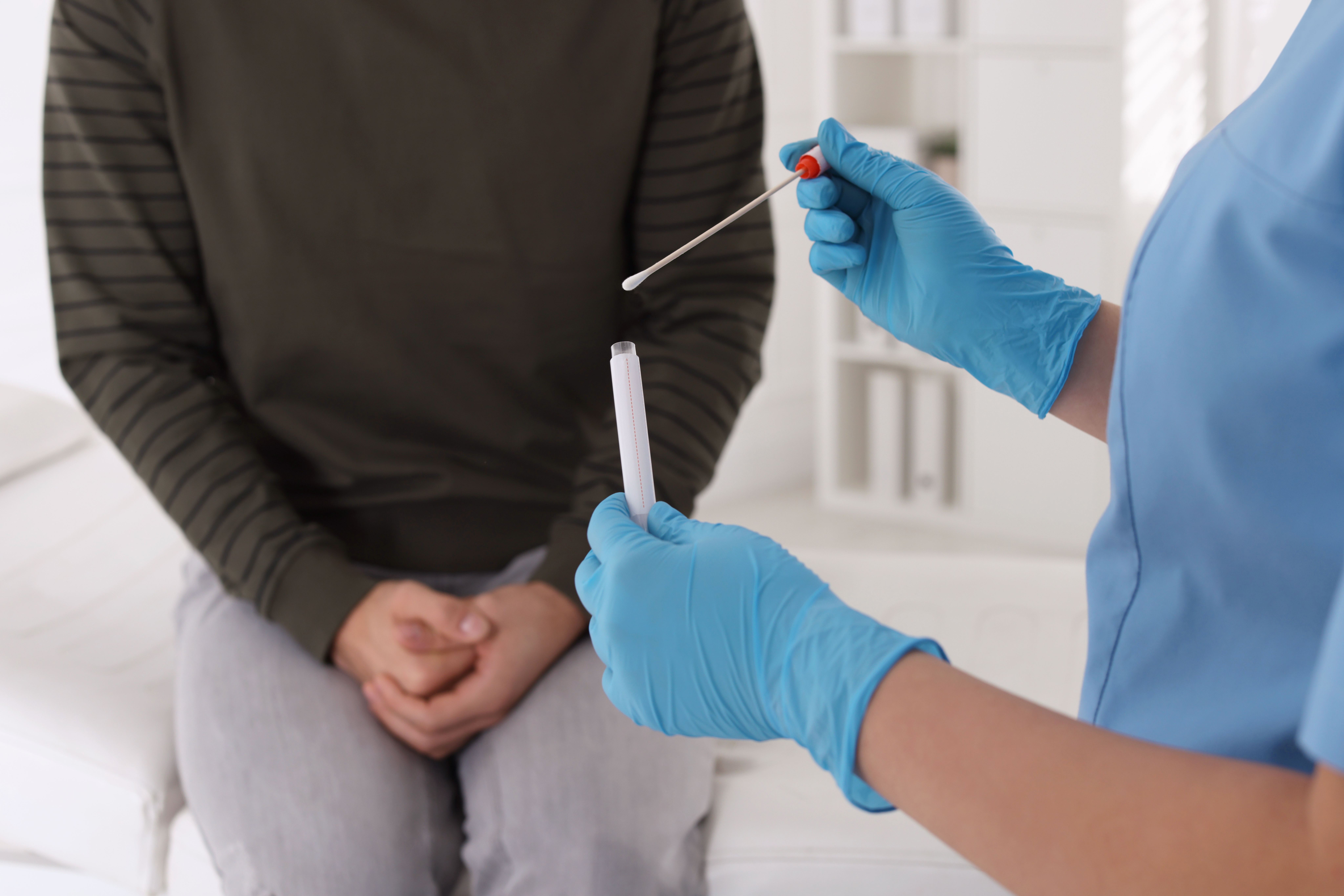Profissional de saúde de luvas azuis segura swab e tubo de coleta diante de paciente sentado, para teste de HPV pós-tratamento